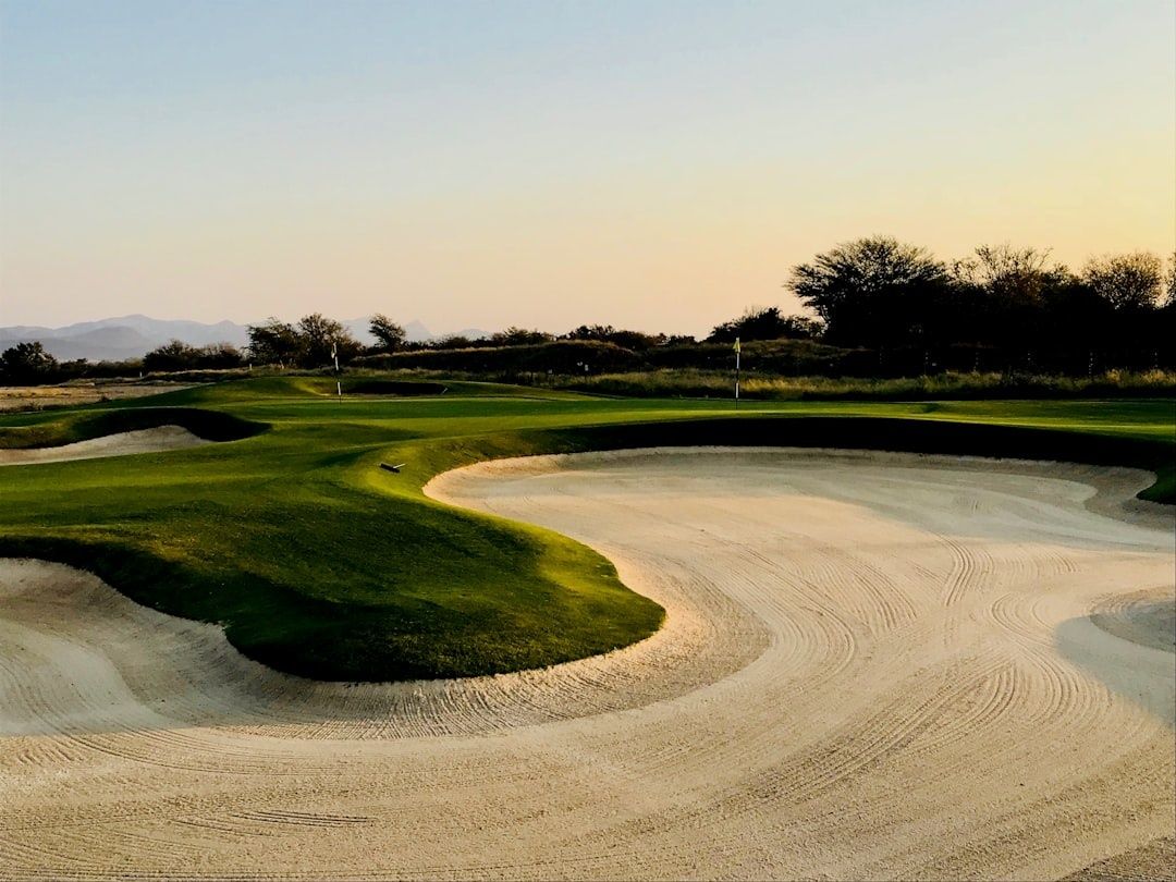 Lugn golfbana med stora bunkrar, greener och flaggor i kvällsljus