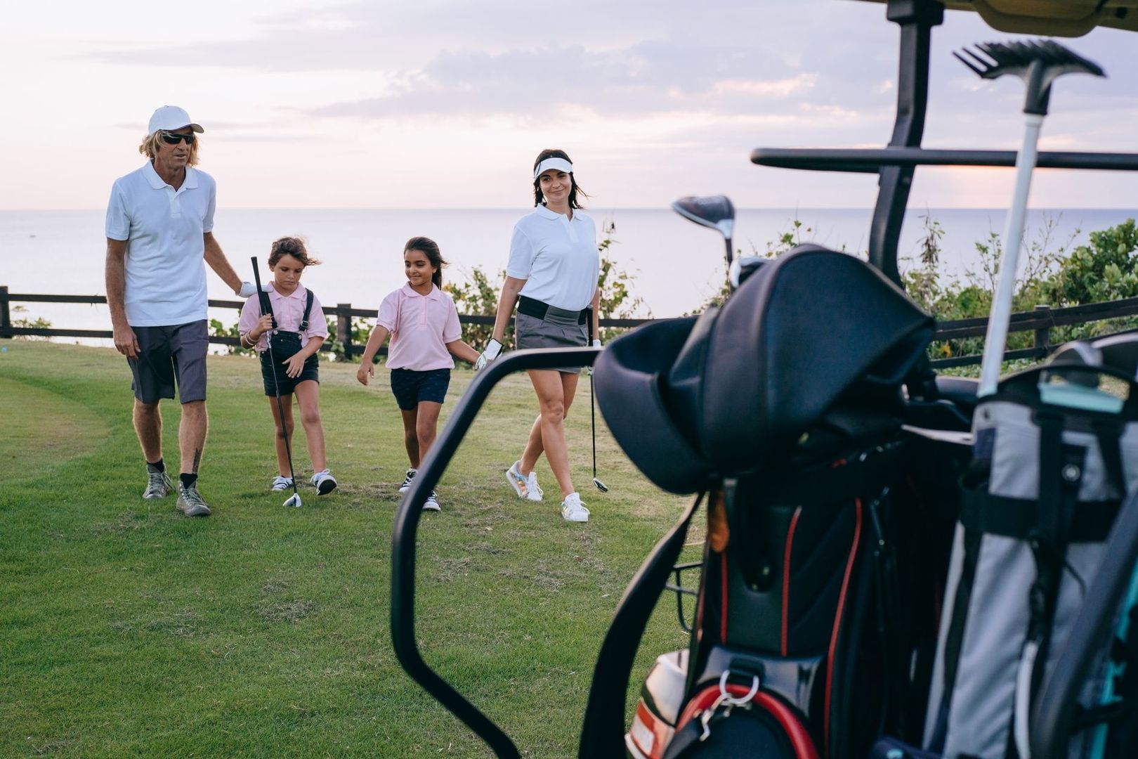 Familj med golfklubbor vid en golfbil och havsutsikt