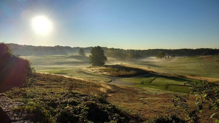 Solbelyst golfbana med morgondimma och böljande grönska